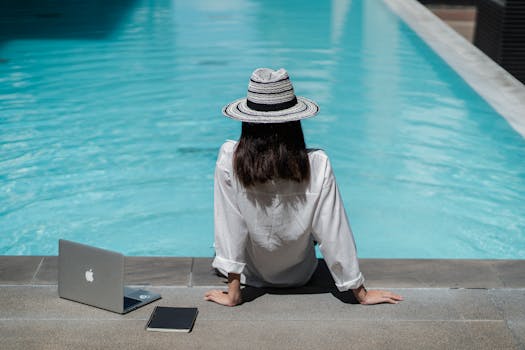 Faceless female freelancer resting at poolside after work on laptop