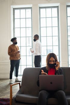 Men Standing Near the Glass Window while Woman Sitting on the Couch using Her Laptop